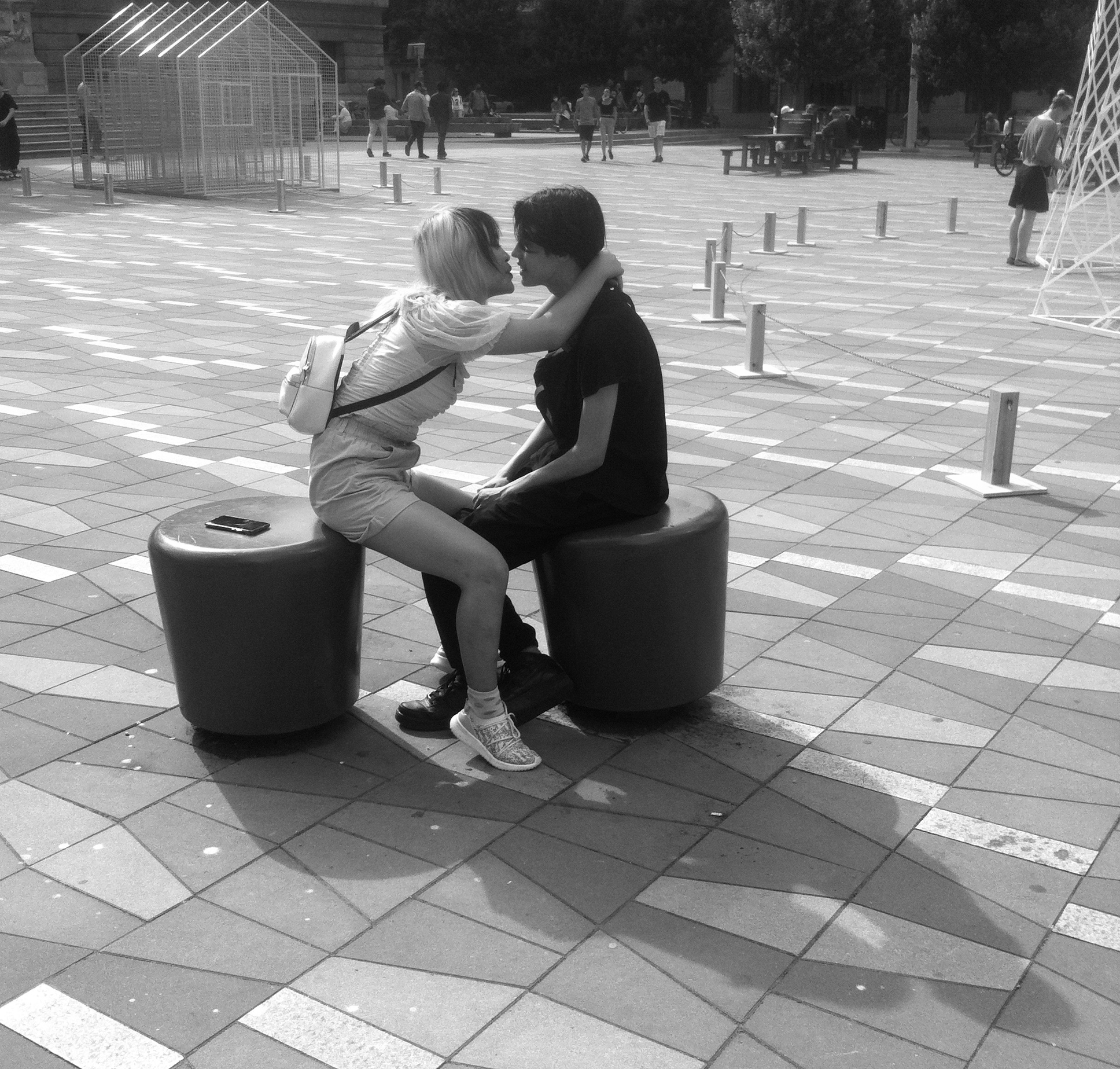 Couple kissing on public square, dark figures against bright pavement